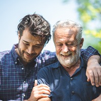 Younger man with arm around shoulder of older man outside in the sun