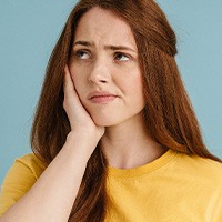 Woman with red hair in yellow shirt holding hand to sore jaw