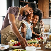 Man, girl, and woman cooking healthy foods together at kitchen island