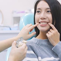Patient pointing to her teeth while dentist examines her smile
