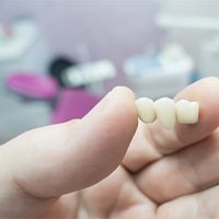 Hand holding dental bridge between finger and thumb