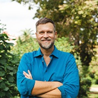 Man in blue button up shirt smiling with arms folded