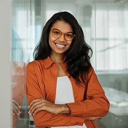 Woman in glasses and orange shirt smiling with arms folded