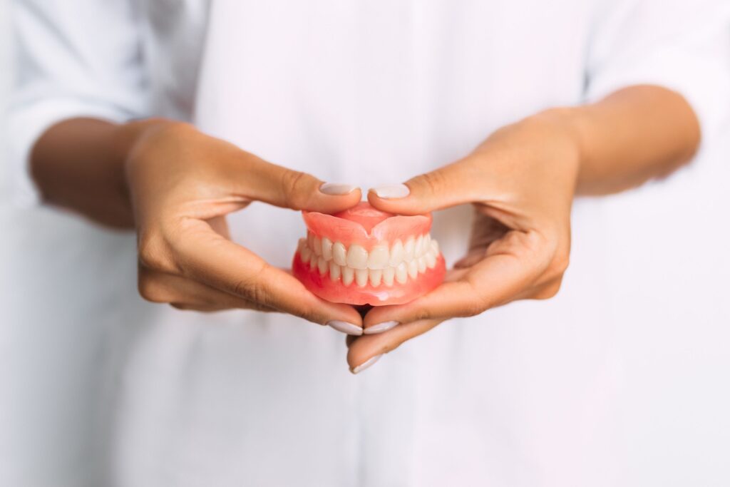 Manicured hands holding a complete set of dentures in front of white jacket